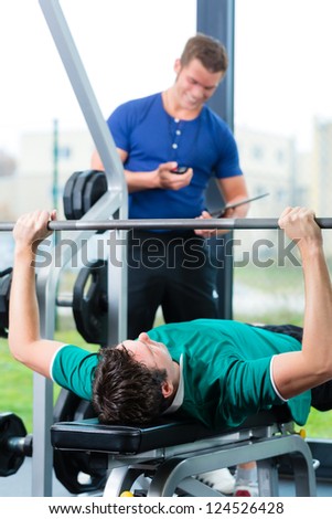 Man with his personal fitness trainer in the gym exercising with dumbbells, he used a barbell on a weight bench