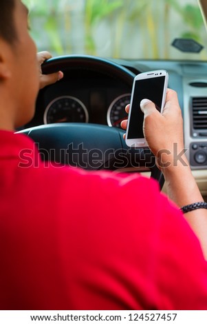 Asian man sitting in car with mobile phone in hand texting while driving