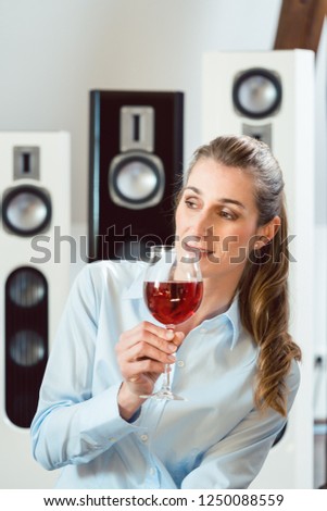 Woman having glass of wine in front of Hi-Fi speakers enjoying the drink and the music
