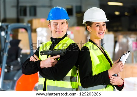Teamwork- Worker or warehouseman with scanner and his coworker with clipboard at warehouse of freight forwarding company