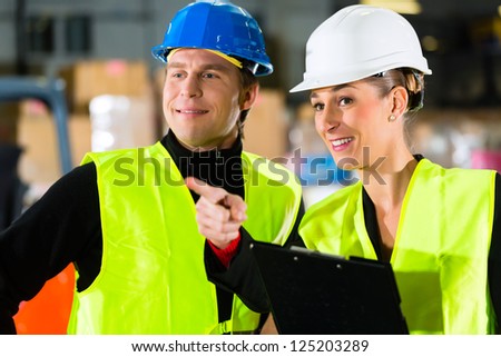Worker or warehouseman and his coworker with clipboard at warehouse of freight forwarding company, pointing