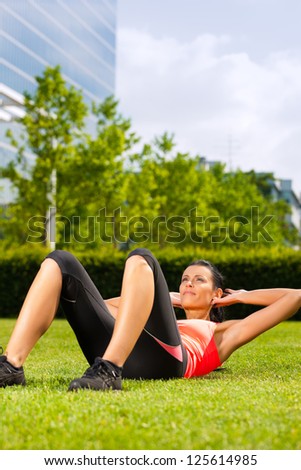 Urban sports - young woman is doing warming up and sit-ups before running in the city