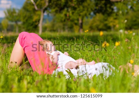 Mother playing with her baby on a great sunny day in a meadow with lots of green grass and wild flowers