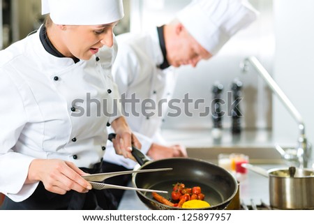 Two chefs - man and woman - in hotel or restaurant kitchen working and cooking in team