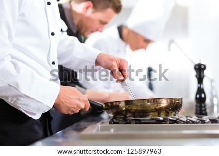 Three Chefs - Men And Woman - In Hotel Or Restaurant Kitchen Working And Cooking In Team