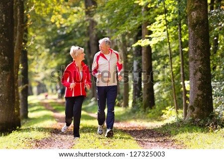 Senior Couple Doing Sport Outdoors, Jogging On A Forest Road In The Autumn