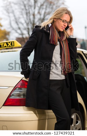 Young woman standing in front of taxi, she gets phone call