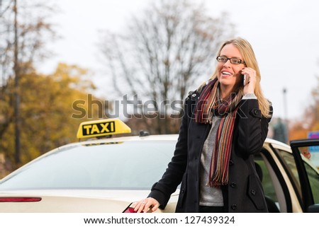 Young woman standing in front of taxi, she gets phone call