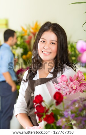 Friendly Asian florist or Saleswoman in a flower shop, holding a flower bouquet