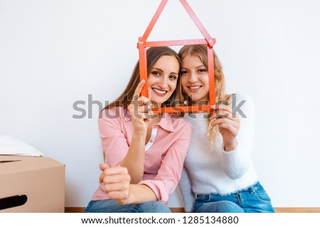 Two women having rented a new apartment moving in looking thru folding rule