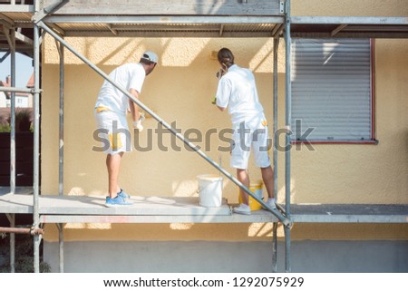 Back view of man and woman painter working coloring wall yellow