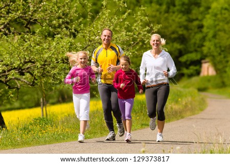 Happy Family with two girls running or jogging for sport and better fitness in a meadow in summer