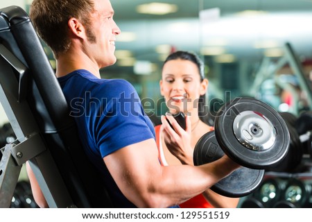 Man or Bodybuilder with his personal fitness trainer in the gym exercising sport with dumbbells, closeup