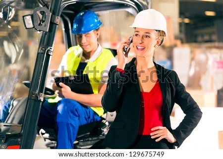 Forklift driver with clipboard at warehouse of freight forwarding company, female super visor or dispatcher with telephone