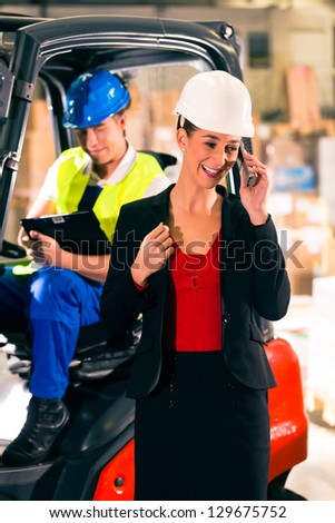Forklift driver with clipboard at warehouse of freight forwarding company, female super visor or dispatcher with telephone