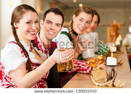 Young people in traditional Bavarian Tracht in restaurant or pub with beer and steins