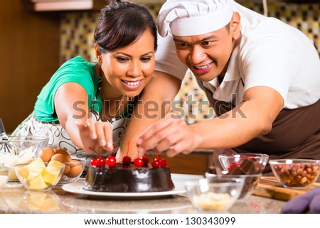 Asian couple baking homemade chocolate cake with cherries  in their kitchen for dessert