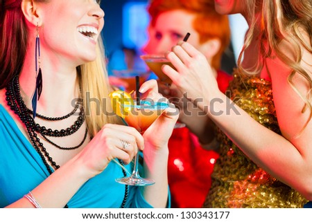 Young women in club or bar drinking cocktails and having fun