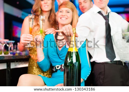 Young people in club or bar drinking champagne and having fun; all are looking into the camera