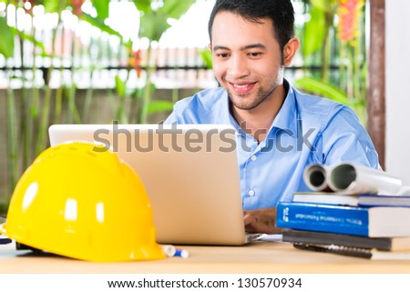 Freelancer - Architect working at home on a design or draft, on his desk are books, a laptop and a helmet or hard hat