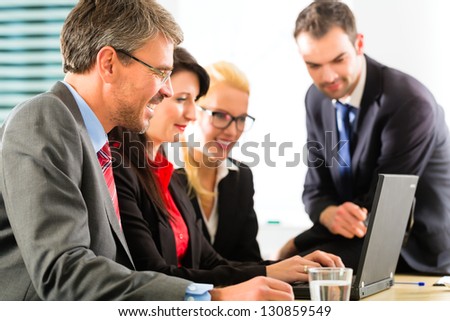 Business - Four professionals in office in business attire looking at laptop screen working together