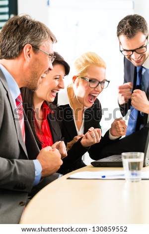 Business - Four professionals in office in business attire looking at laptop screen working together, they rejoice
