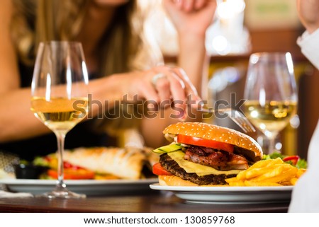 Couple - Man And Woman - In A Fine Dining Restaurant They Eat Fast Food, Burger And Fries, Closeup