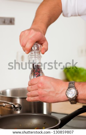 Man in the kitchen - only hands to be seen - is adding spices to food