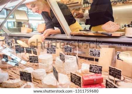 Shop clerk woman sorting cheese in the supermarket display to sell it