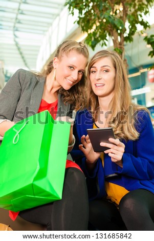 Two female friends having fun while shopping in a mall, they bought a e-book