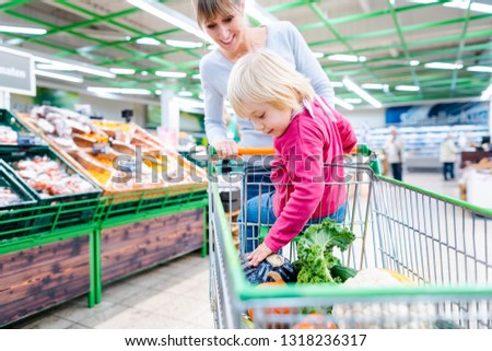 Mother having her toddler girl riding in shopping cart of supermarket