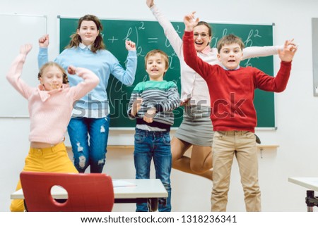 Teacher and students of primary school jumping in classroom raising their arms