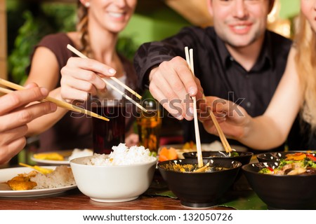 Young people eating in a Thai restaurant they eating with chopsticks Young people eating in a Thai restaurant they eating with chopsticks