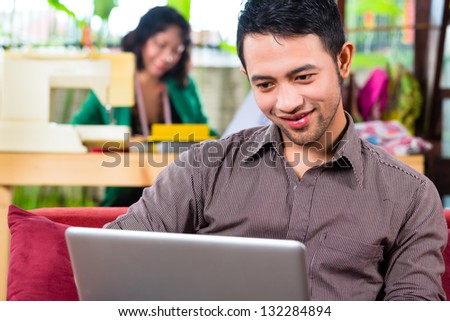 Freelancer - Fashion designer working at home on a design or draft, her boyfriend sitting with a laptop on the couch