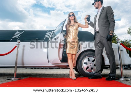 Driver helping VIP woman or star out of limo on red carpet to a reception