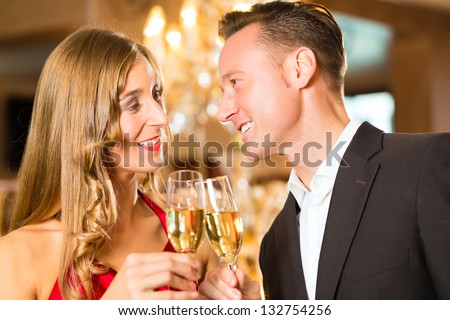 Couple, man and woman, drinking champagne in a fine dining restaurant, each with glass of sparkling wine in hand