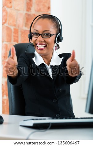 Young businesswoman or secretary working in her Office, she sitting on the desk in front of the window and working on a computer with a headset, she has a customer pitch