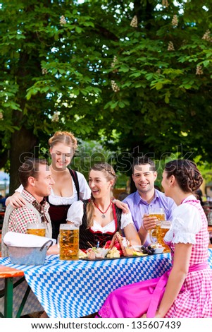 In Beer garden - friends Tracht, Dirndl and on a table with beer and snacks in Bavaria, Germany