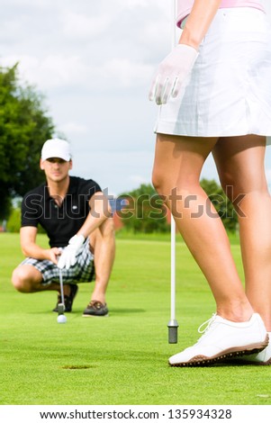 Young sportive couple playing golf on a golf course, he is putting at the green, close-up