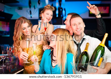 Young people in club or bar drinking champagne and having fun; one man is looking into the camera