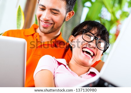 Young Indonesian couple - man and woman - sitting with laptops on a couch