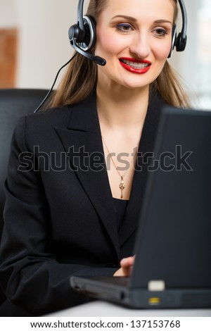 Young businesswoman or secretary working in her Office, she sitting in front of the window and working on a computer with a headset, she has a customer pitch