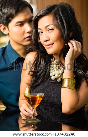 Asian man and woman in flirting intimately at bar drinking cocktails