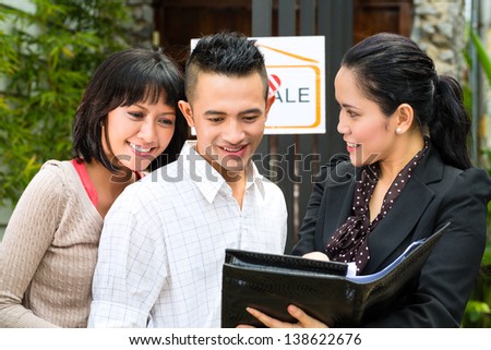 Real estate market - young Indonesian couple looking for real estate apartment or house to rent or buy, the realtor showing a document