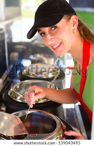 Female owner of a soup kitchen or a field kitchen stirs with a ladle in the soup