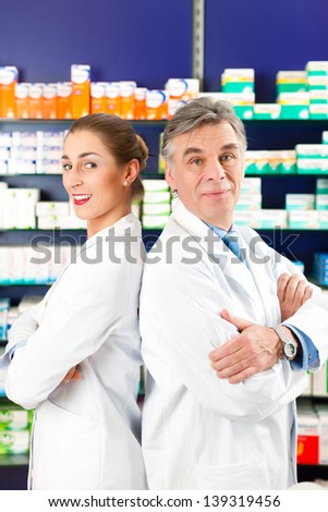 Two Pharmacists standing in pharmacy or drugstore in front of shelves with pharmaceuticals