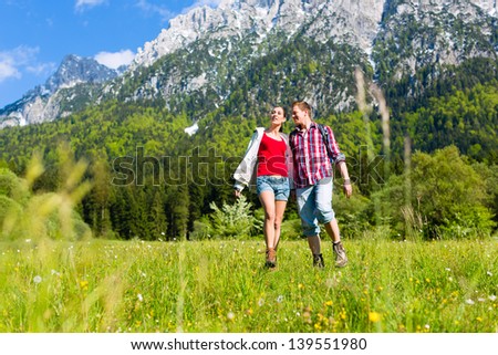 Happy couple walking on the grass in front of mountain panorama