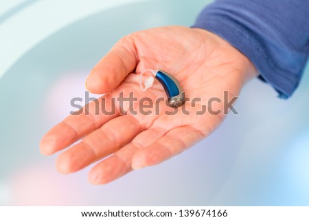Closeup of a hand holding small inconspicuous hearing aid, such as deaf people need it