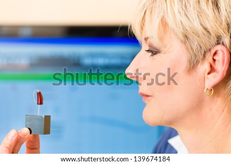 Older woman or female pensioner with hearing problem taking a hearing test, she holding model of hearing aid