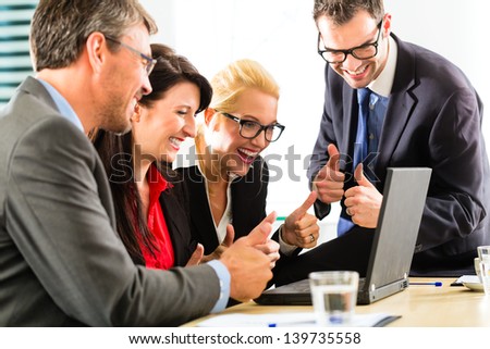 Business - Four professionals in office in business attire looking at laptop screen working together, they rejoice